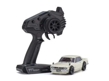 De afbeelding toont een witte modelauto, een Nissan Skyline 2000 GT-R KPGC10, naast een zwarte afstandsbediening. De afstandsbediening heeft een stuurwiel en trekker voor bediening.