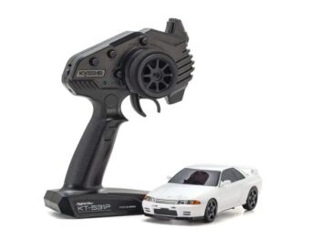De afbeelding toont een witte miniatuur raceauto, waarschijnlijk een Nissan Skyline GT-R Nismo R32, naast een zwarte afstandsbediening. De auto heeft een sportief design met donkere ramen en zwarte velgen.
