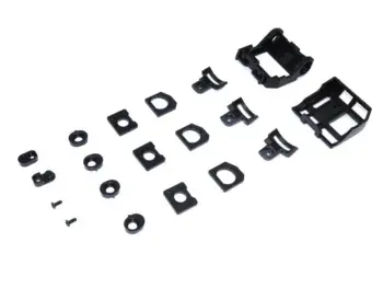 The photograph shows a set of black plastic parts, including two larger housings and various smaller rings, plates and screws. The parts are scattered across a white background.
