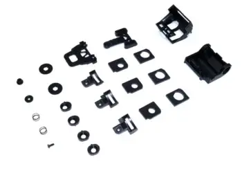The image shows a set of black plastic parts of various shapes and sizes, including larger housings, smaller fasteners, rings, screws and two small springs, scattered across a white background.
