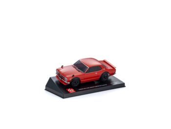 Un coche de juguete rojo, un Nissan Skyline 2000 GTR, se encuentra sobre un soporte de exposición negro. Se trata de una réplica muy detallada con llantas negras y un alerón trasero.