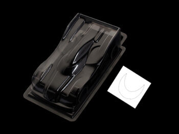 De afbeelding toont een transparante, ongeverfde lexaan body voor een RC auto, met een gestroomlijnd ontwerp. Naast de body ligt een klein wit velletje met een halvemaanvormige contour.