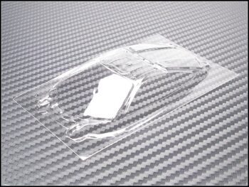 De afbeelding toont een transparant, voorgevormd lexan raam voor een modelauto. Het is helder en heeft de contouren van een autoruit, liggend op een grijze ondergrond met een koolstofvezelpatroon.