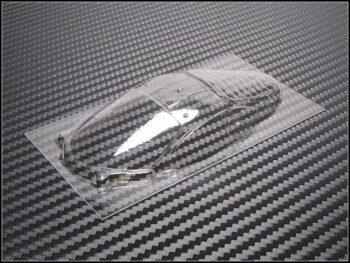 Op de foto is een transparant, voorgevormd lexan raamwerk te zien, liggend op een donkere ondergrond met een koolstofvezelpatroon. Het raamwerk heeft de vorm van een autocarrosserie, met duidelijke contouren voor ramen en een dak.