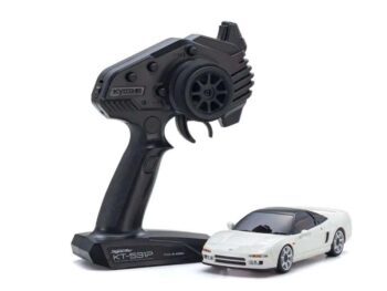 De afbeelding toont een witte modelauto, waarschijnlijk een Honda NSX, naast een zwarte afstandsbediening. De afstandsbediening heeft een stuurwiel en een trekker voor de bediening.