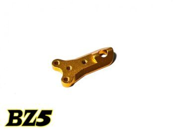 De afbeelding toont een goudkleurig metalen onderdeel met een onregelmatige vorm en meerdere schroefgaten. Het lijkt een onderdeel voor een modelauto te zijn.
