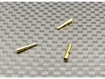 De afbeelding toont drie kleine, goudkleurige metalen stekkers met een cilindrische vorm en een licht taps toelopend uiteinde. Ze liggen verspreid op een donkergrijze ondergrond met een ruitpatroon.