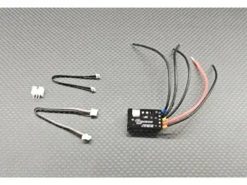 Op de foto is een compacte, zwarte elektronische snelheidsregelaar (ESC) te zien met diverse draden in zwart en rood. Er liggen ook enkele losse witte connectoren en zwarte en rood/witte kabels naast op een grijze, gestructureerde ondergrond.