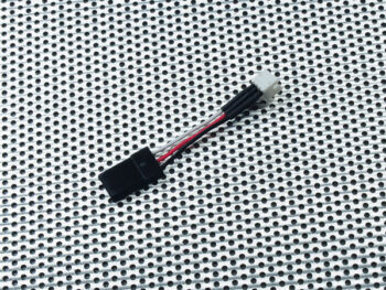 De afbeelding toont een adapterkabel met een zwarte connector aan het ene uiteinde en een witte connector aan het andere uiteinde, verbonden door drie gekleurde draden (zwart, rood, wit/grijs). Het product ligt op een geperforeerde metalen ondergrond.
