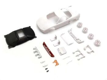 De foto toont een witte auto body met losse onderdelen, waaronder een zwart dak en wielen. De onderdelen zijn van plastic en liggen verspreid op een witte achtergrond.