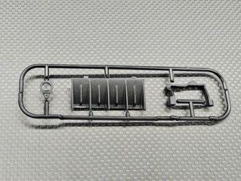 De foto toont een zwart kunststof frame met verschillende onderdelen, waarschijnlijk voor een modelauto. De onderdelen zijn gegoten en bevatten een diffuser en servo mount.
