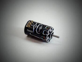 De foto toont een zwarte motor met zilverkleurige accenten en een uitstekende as. De motor heeft een cilindrische vorm en is voorzien van diverse aansluitingen.