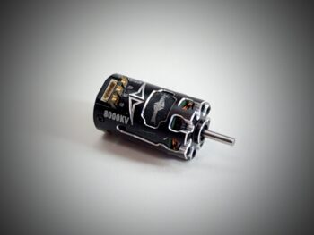 De foto toont een zwarte motor met zilverkleurige accenten en een zilverkleurige as. De motor heeft een cilindrische vorm en is voorzien van diverse aansluitingen.