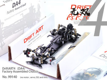 The photograph shows a black chassis of a model car, packaged in a white box with red and black text. The chassis has various metal parts and gold accents.