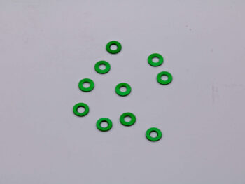 De foto toont een aantal groene ringvormige shims. De shims liggen verspreid op een witte ondergrond.