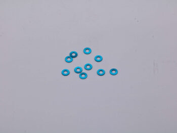 De foto toont een aantal kleine, blauwe ringen. De ringen lijken van metaal te zijn gemaakt en liggen verspreid op een grijze ondergrond.