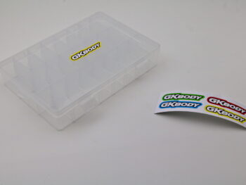 De afbeelding toont een transparante opbergbox met 24 compartimenten. Naast de box liggen stickers met het GKBODY logo.