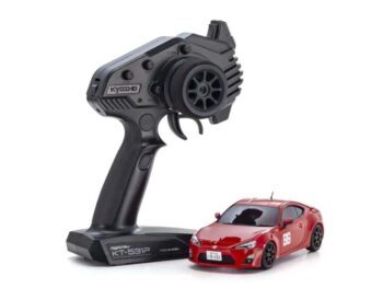 De foto toont een rode modelauto met een zwarte afstandsbediening. De auto heeft zwarte wielen en de afstandsbediening heeft het Kyosho logo.