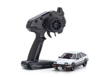De foto toont een witte modelauto met zwarte details en een zwarte afstandsbediening. De auto heeft een herkenbare vorm en de afstandsbediening heeft het Kyosho logo.