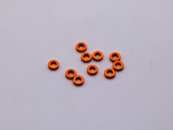 De foto toont een aantal oranje ringvormige shims. De shims liggen verspreid op een witte ondergrond.