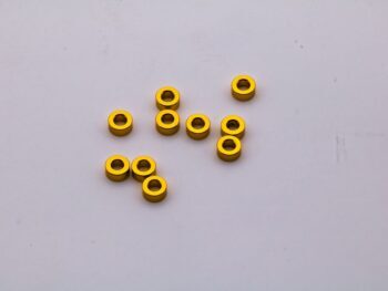 De foto toont een aantal gele ringvormige shims. Ze liggen verspreid op een witte ondergrond.