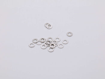 De foto toont een verzameling zilverkleurige ringen, vermoedelijk shims, verspreid over een witte achtergrond. De ringen zijn van metaal en hebben een ronde vorm met een gat in het midden.