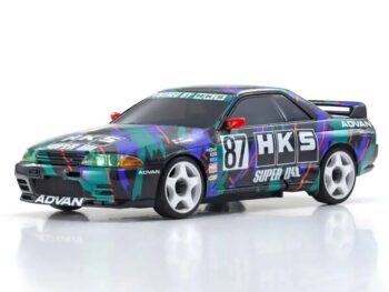 De foto toont een modelauto van een Nissan Skyline GT-R R32, met een opvallende kleurstelling van groen, blauw en paars. De auto heeft witte velgen en diverse sponsorlogo's.