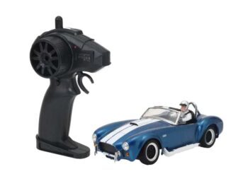 De afbeelding toont een blauwe RC-auto, een replica van een Shelby Cobra 427 S/C, met witte racestrepen op de motorkap en het dak. Naast de auto ligt een zwarte afstandsbediening.