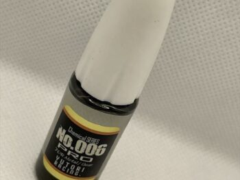 De foto toont een flesje olie met een witte dop en een zwarte onderkant. De fles heeft een label met gele en zwarte accenten.