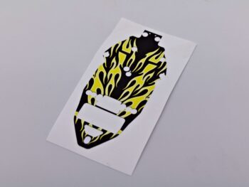 De foto toont een sticker met een zwart basisontwerp en gele vlammen. De sticker is uitgesneden in een vorm die lijkt op een chassis.