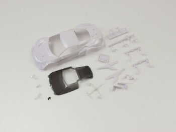 De foto toont een witte auto body en diverse losse onderdelen. Er is ook een donkergrijze dak onderdeel te zien.