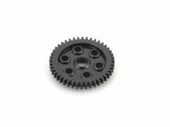 The photograph shows a black gear wheel with sharp teeth around the edge and holes in the centre. The gear wheel is made of a dark material and is placed on a white background.