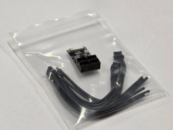 De afbeelding toont een kleine zwarte elektronische ontvanger met meerdere connectoren, samen met een bundel zwarte kabels, verpakt in een doorzichtige plastic zak.