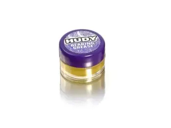 De foto toont een klein potje met paarse deksel en een gele substantie erin. Op de deksel staat de merknaam 'Hudy' en de productnaam 'Bearing Grease'.