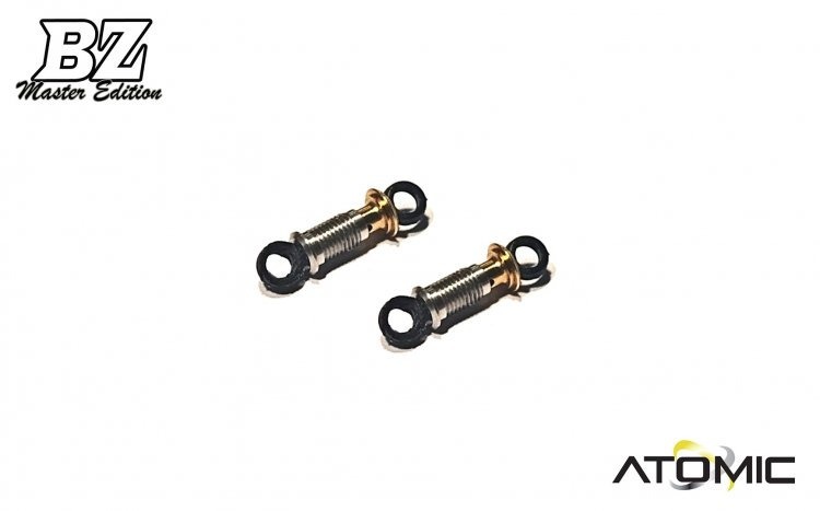 twee rc auto schokdempers met gouden accenten De afbeelding toont twee korte metalen dempers met gouden accenten en zwarte ophangingen. Er is een 'BZ Master Edition' logo linksboven en een 'ATOMIC' logo rechtsonder.