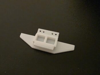 De afbeelding toont een wit, 3D-geprint onderdeel dat lijkt op een body mount met een bumper. Het heeft meerdere gaten aan de bovenkant en twee vierkante uitsparingen.