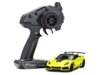 De foto toont een gele modelauto met een zwarte afwerking en een zwarte afstandsbediening. De auto heeft een sportieve vorm en de afstandsbediening heeft het Kyosho logo.