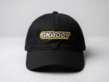 Een zwarte GKBODY pet met geel en grijs logo, vooraanzicht, passend bij de GKBODY GK70001 Lexan Body 98mm voor 1/28 Mini-Z.