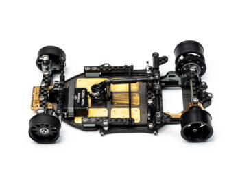 Gedetailleerd RC-auto chassis met carbon fiber onderdelen, messing gewichten en een zwarte Torq servo op wit.