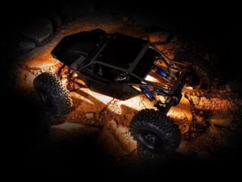 Zwarte RC rock crawler op rotsachtige ondergrond in het donker met warme onderverlichting.